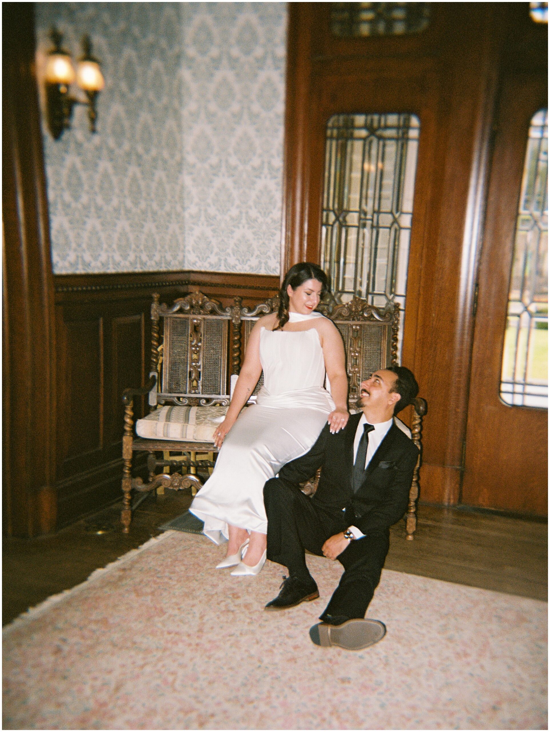 Bride in a carved chair with groom at her feet, Alexander Mansion engagement session