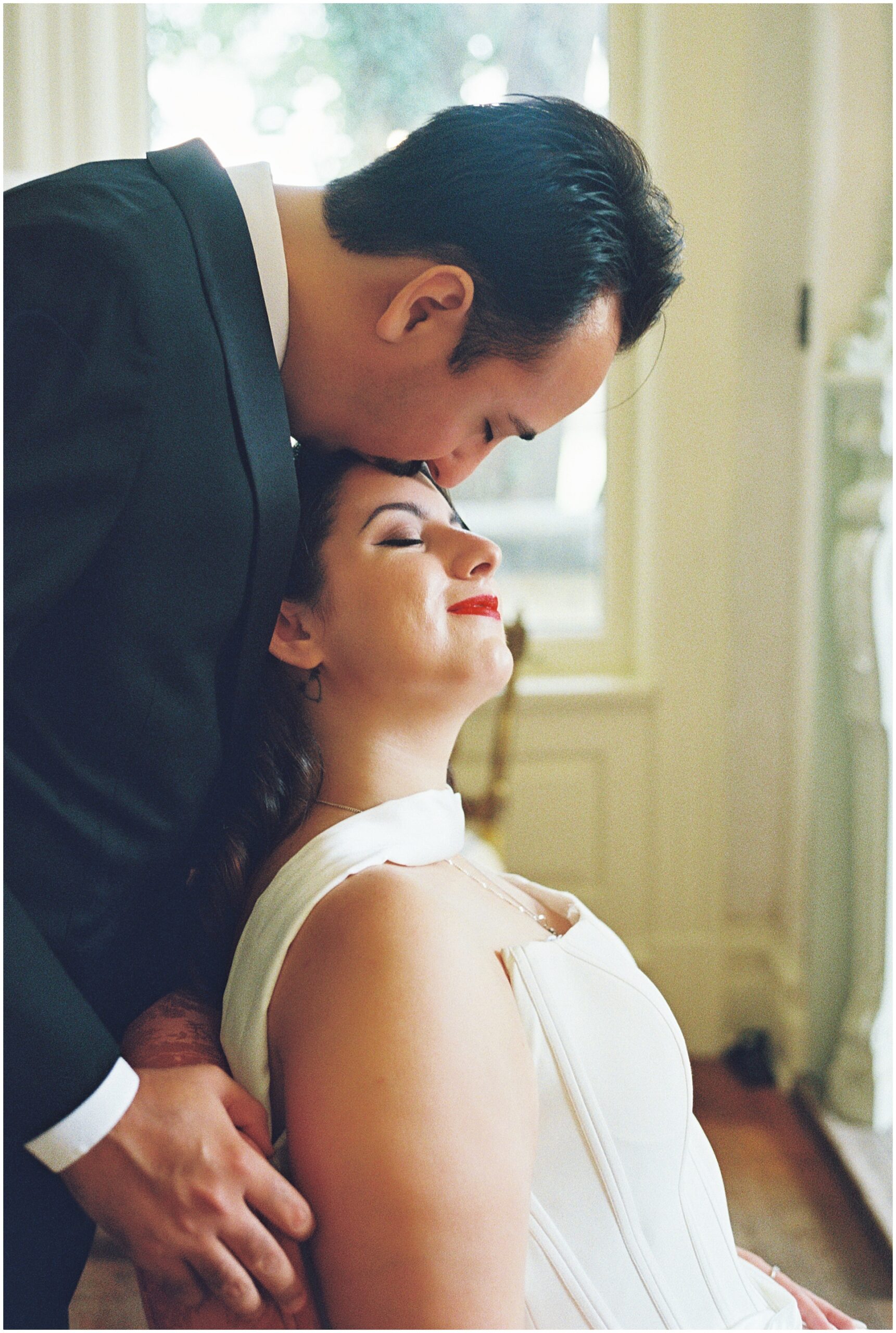 Groom kissing bride's forehead in the Alexander Mansion parlor, 35mm film