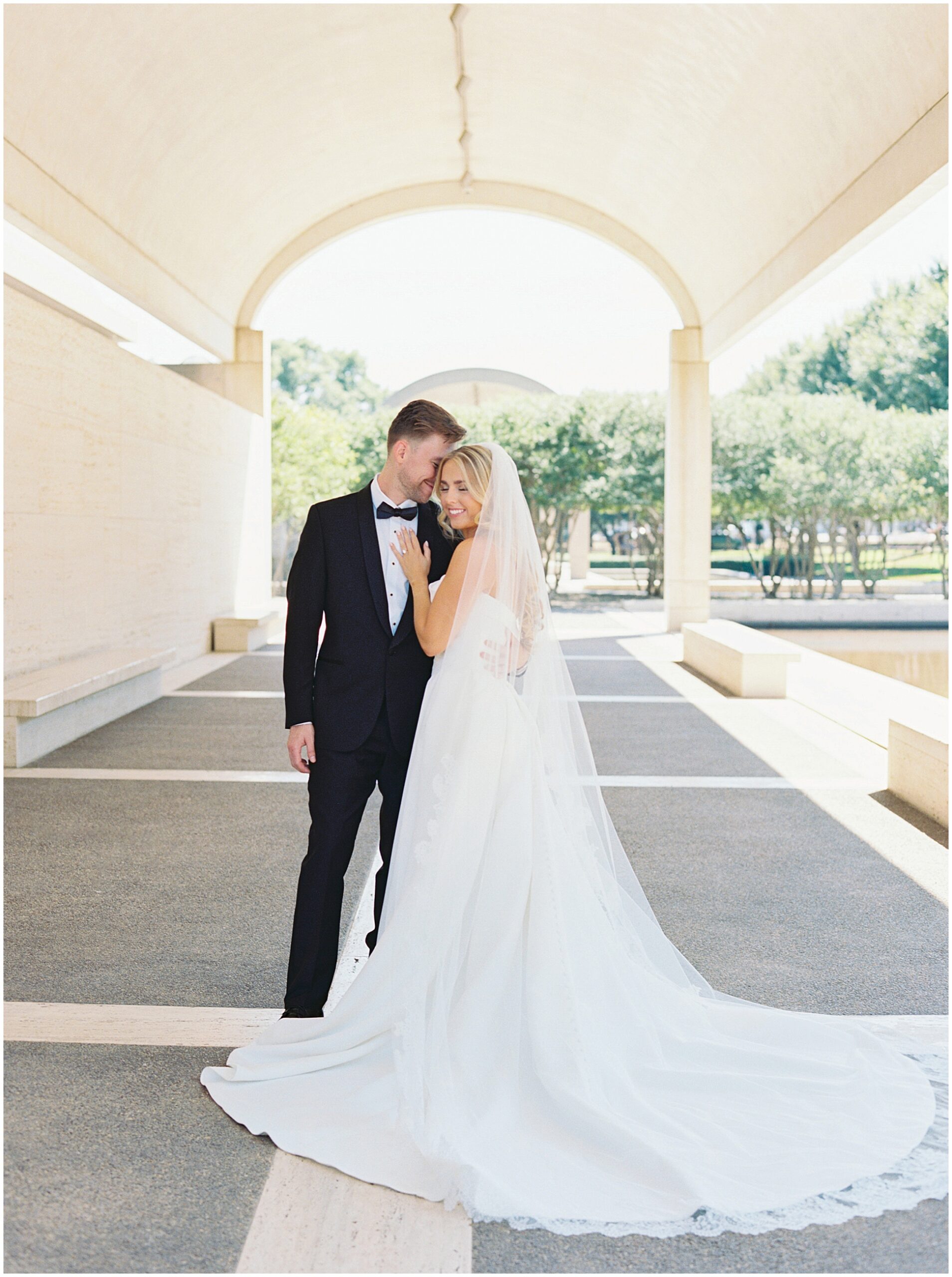 Bride in a cathedral veil and groom in a black tuxedo at the Kimbell Art Museum in Fort Worth