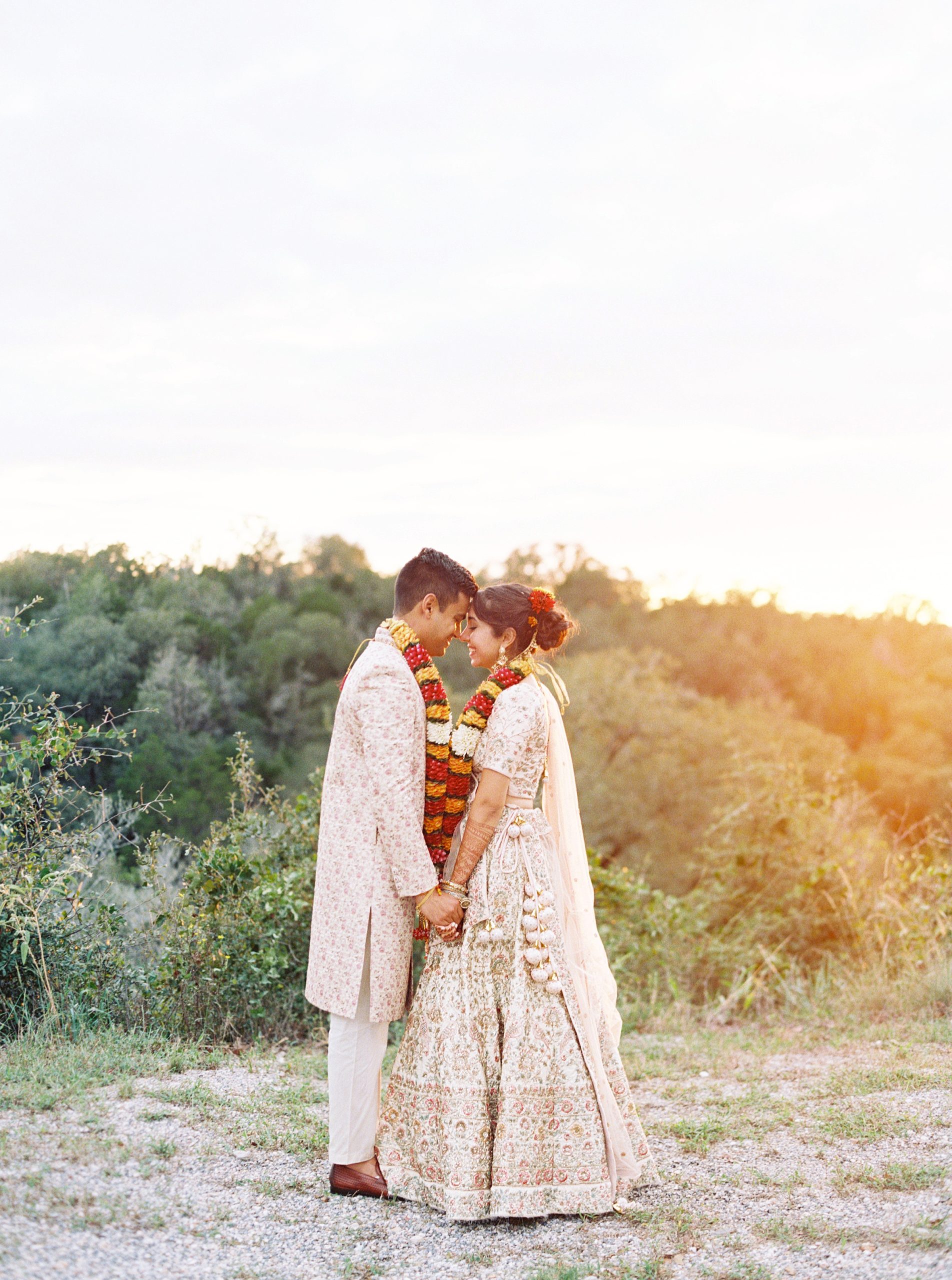 indian bride and groom wearing traditional sari and salwar holding hands during sunset at Shiraz Gardens in Bastrop