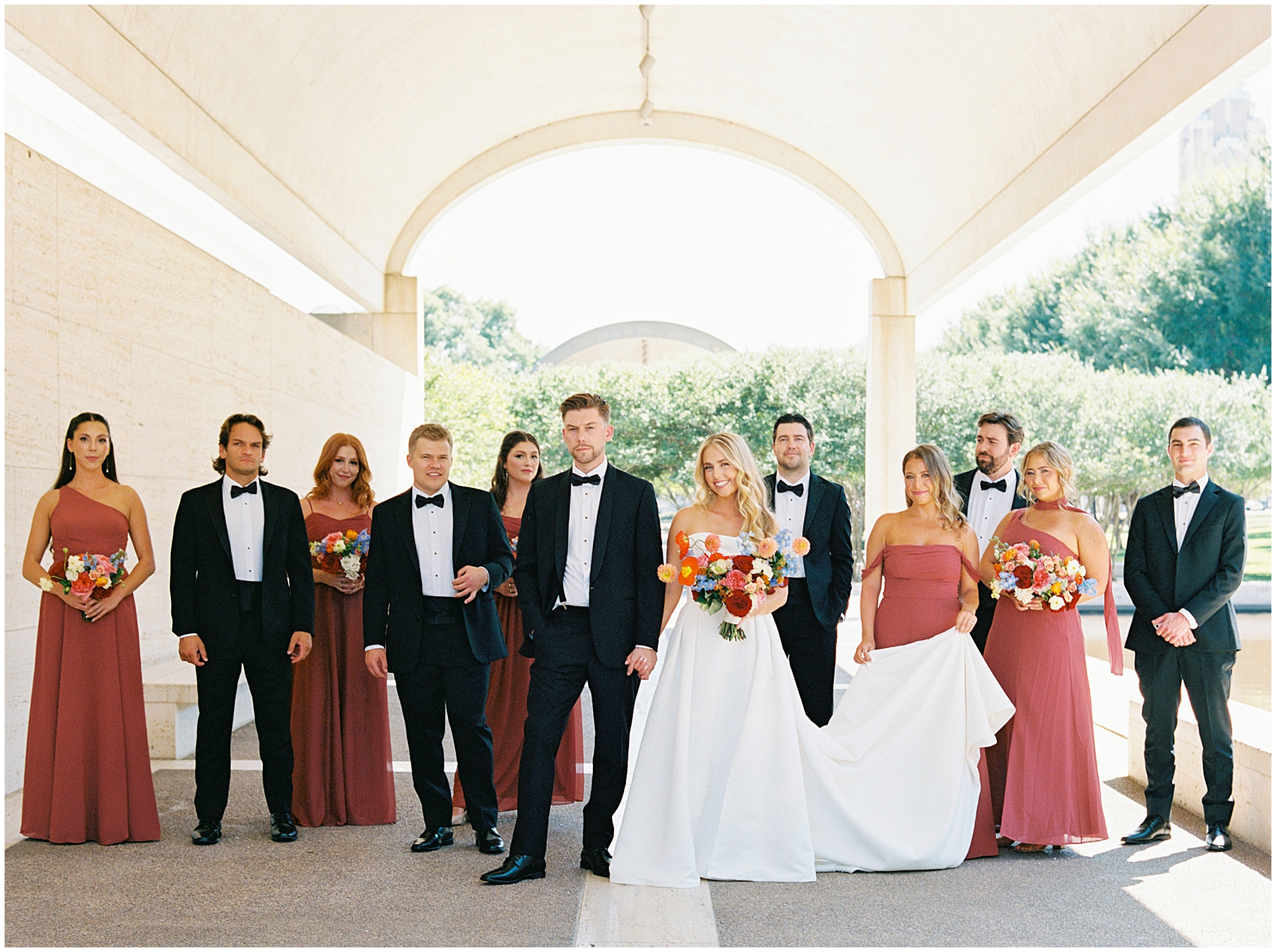 wedding party dressed in autumn colors under arches at kimball museum